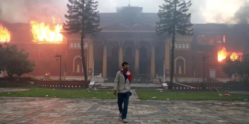 Um homem envolto na bandeira nacional do Nepal foi visto diante do incêndio que atingiu o gabinete da Presidência, em Katmandu - Foto: Anup OJHA / AFP